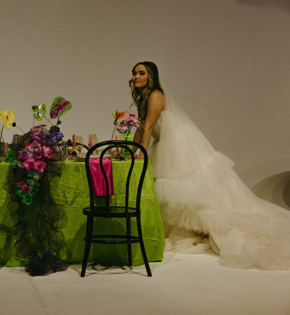 A person in a wedding dress with their arms leaning on a reception table. 